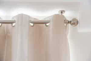 Eyelet curtains hung on a silver curtain pole with ball finial. The pole is ceiling mounted